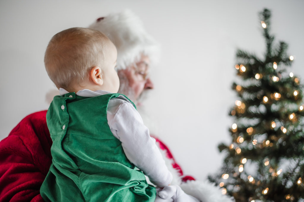Santa Claus holding bay boy in front of Christmas tree during 2020 Santa Mini photo session