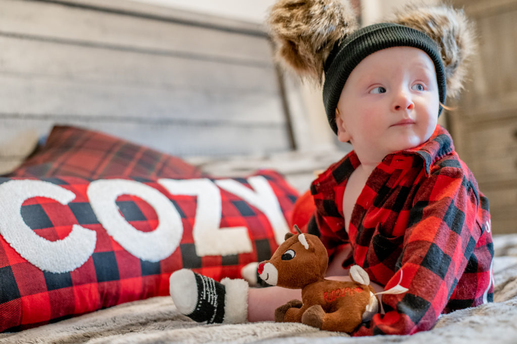 Baby boy on bed playing with Christmas toy reindeer during a “Home for the Holidays” Santa Session