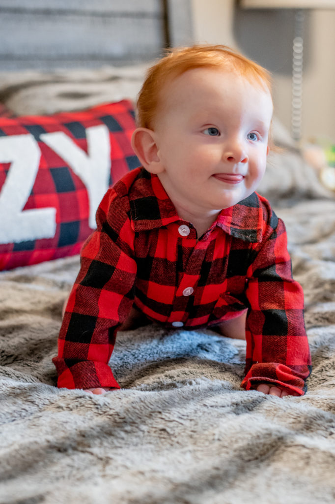 Baby boy in Christmas outfit crawling on bed during a “Home for the Holidays” Santa Session