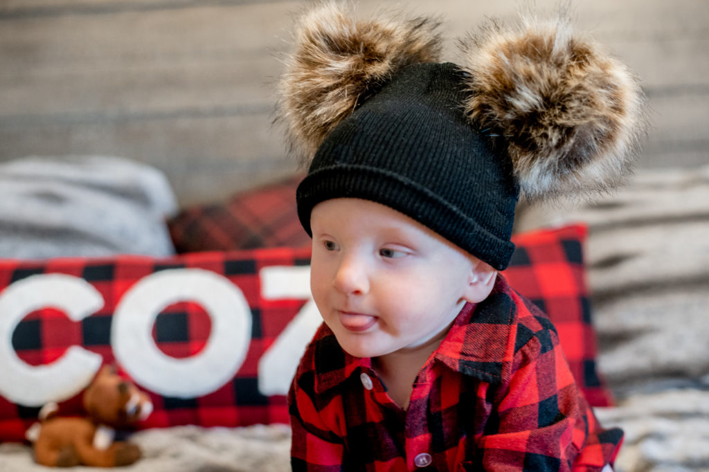 Baby boy in Christmas outfit and hat on bed during a “Home for the Holidays” Santa Session