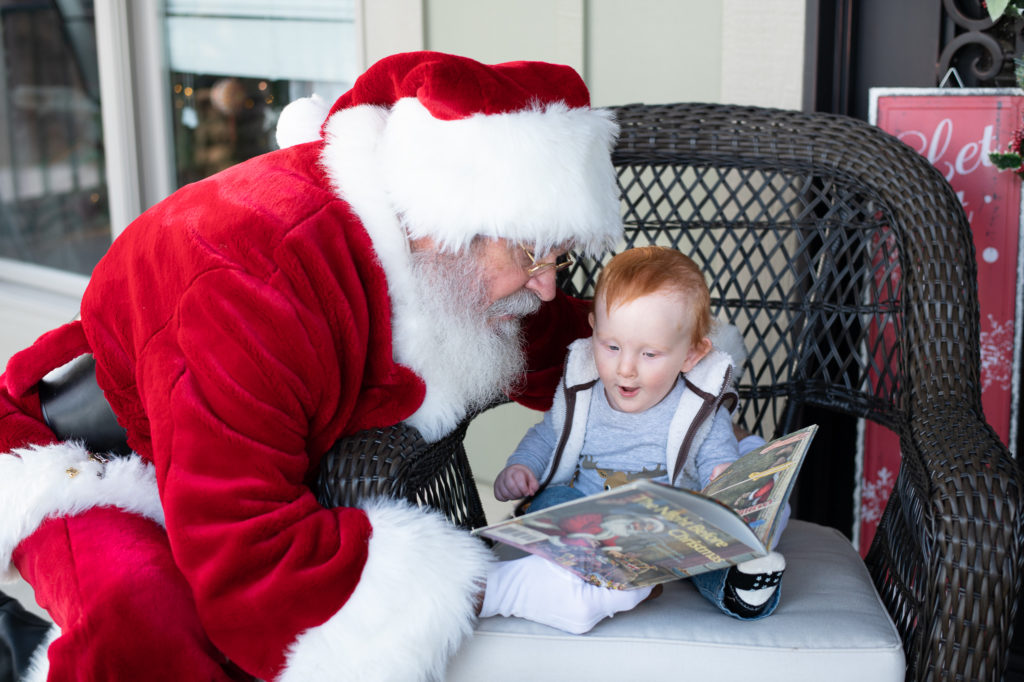 Santa and baby boy reading a Christmas book on front porch during a “Home for the Holidays” Santa Session