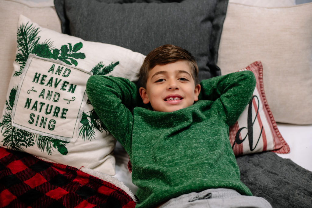Christmas photo of a young boy lying on a bed with pillows.