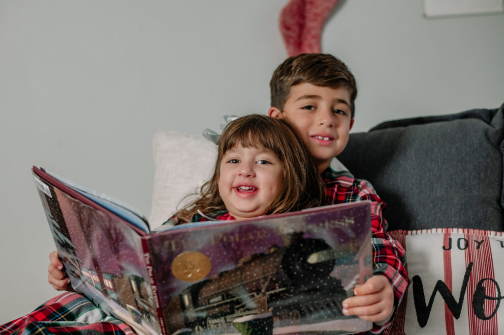 Siblings in matching Christmas pajamas reading a Christmas story 
