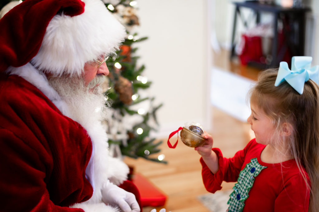 Little girl looking at toy with candy that Santa has giving her during "Home for the Holidays" Santa session