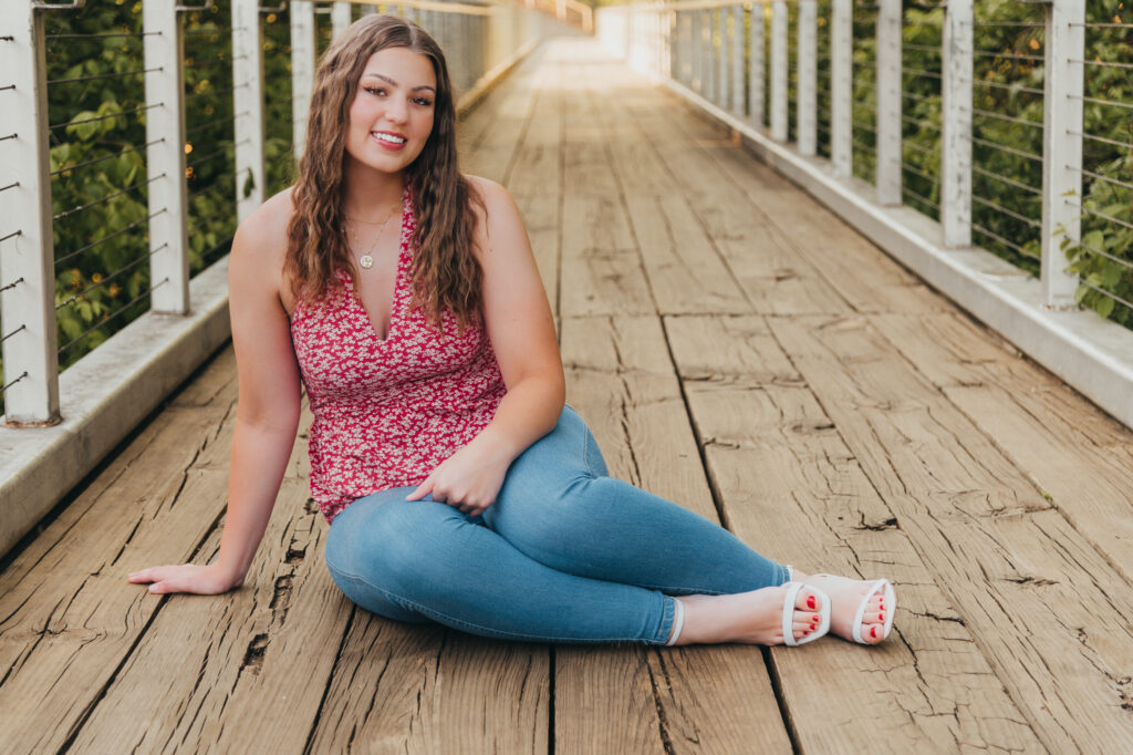 What to Wear for Your Senior Pictures – Seasonal Outfit Ideas for high school Seniors - Chattanooga senior girl in floral spring top with light wash denim jeans and white heels sitting on bridge at Renaissance Park in downtown Chattanooga, TN